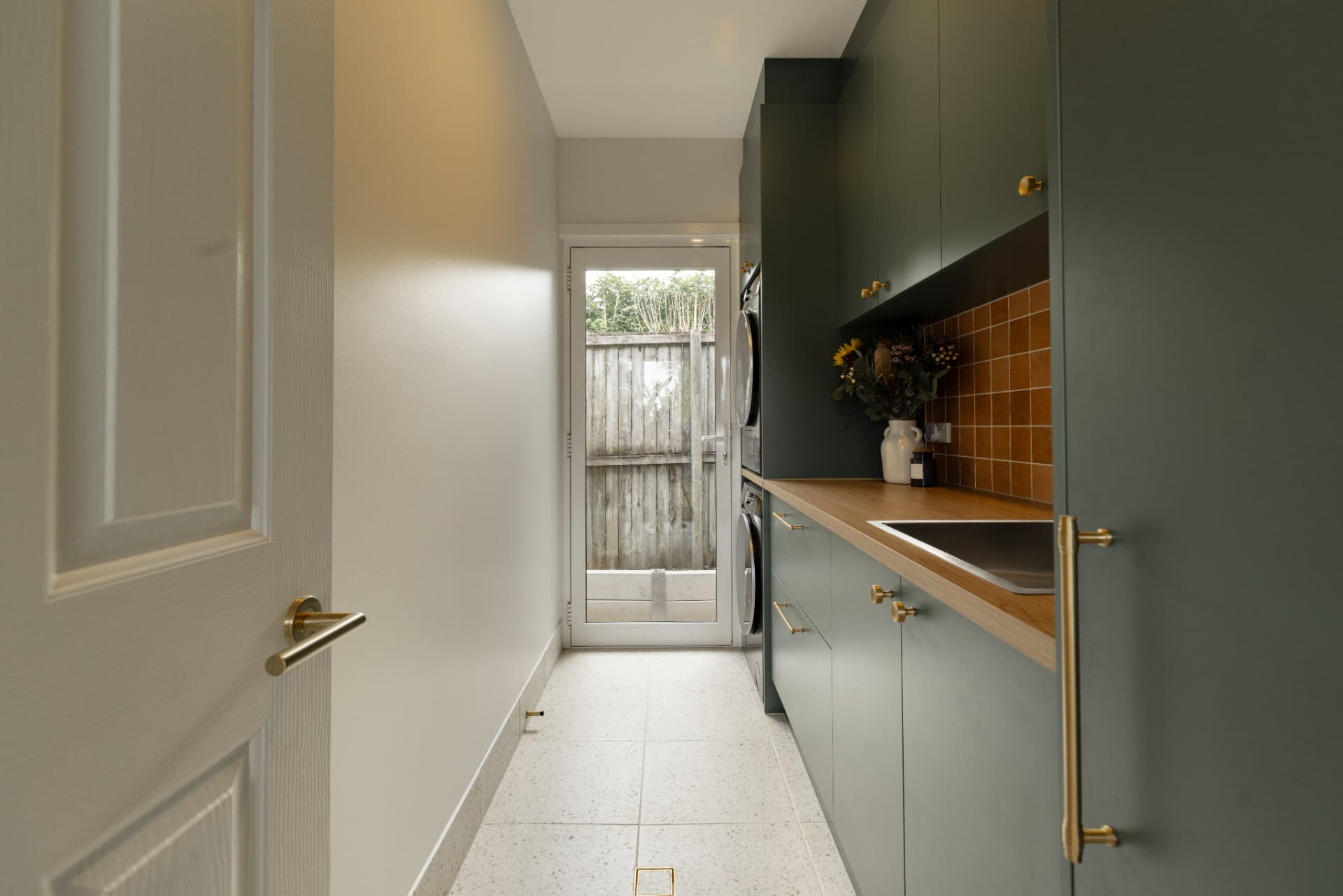 Custom laundry with deep green joinery, timber benchtop and terracotta tiled splashback.