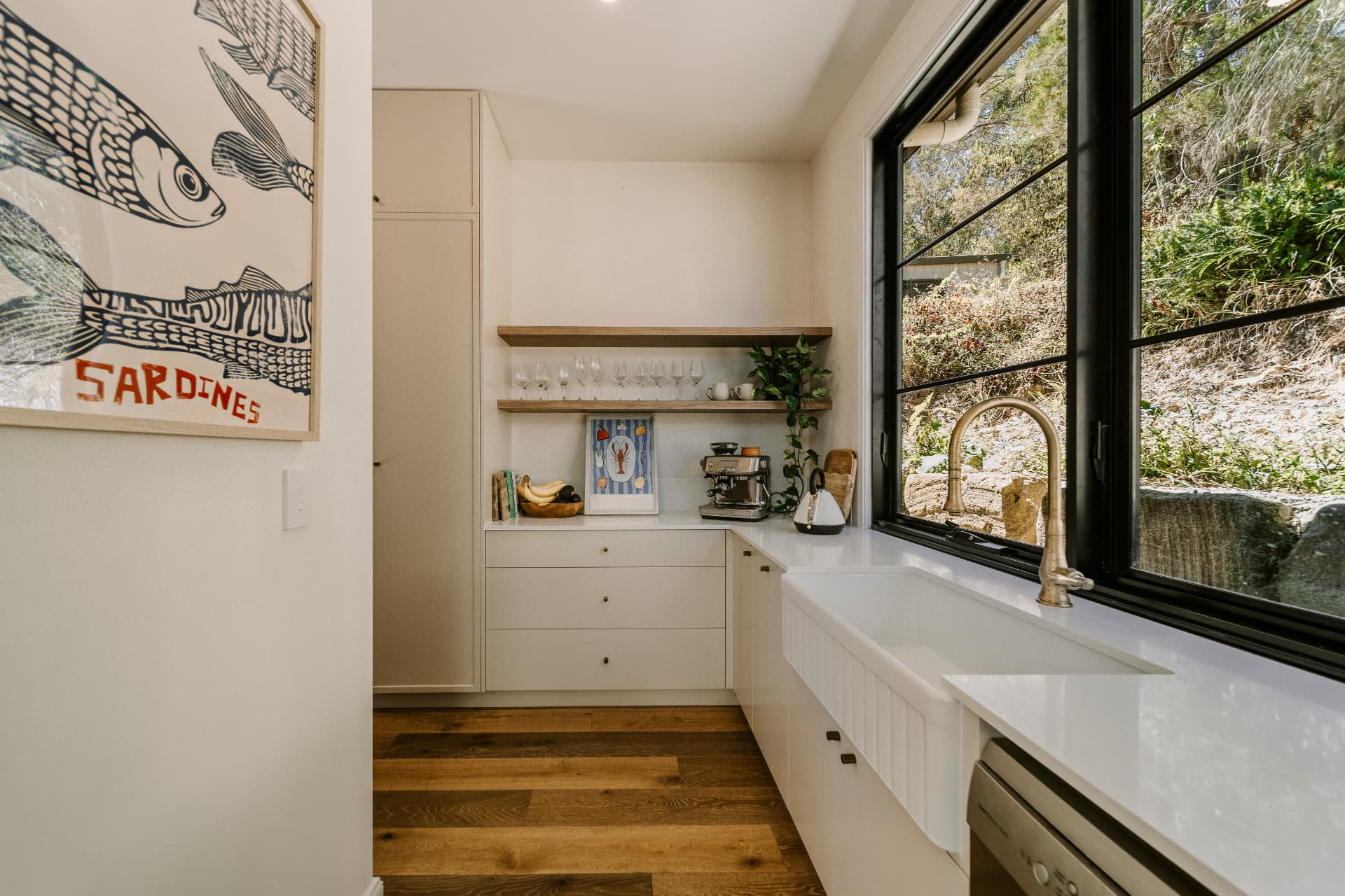 Butler's pantry with farmhouse sink, open timber shelving and black framed window.