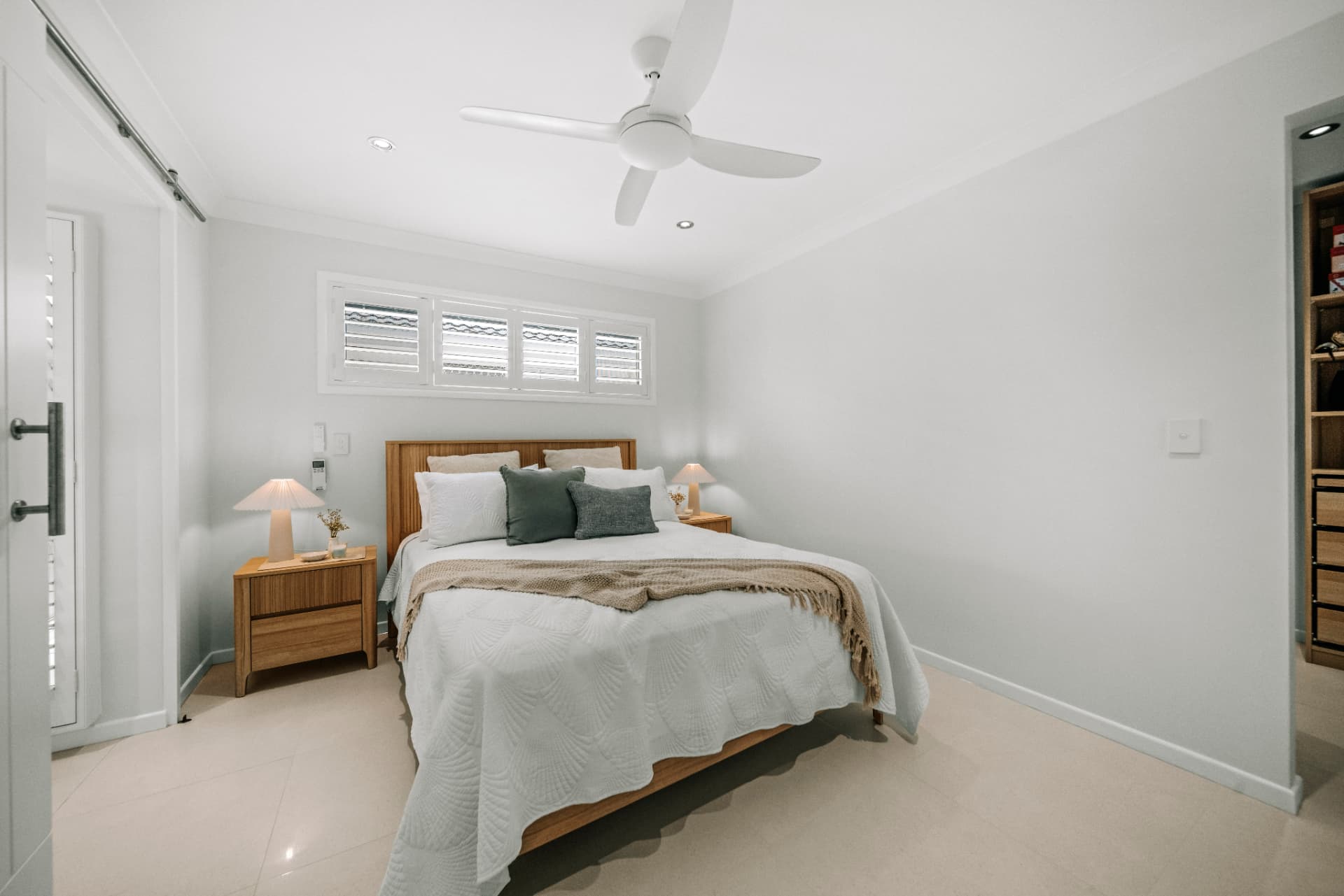 Coastal bedroom with plantation shutters and timber bedside joinery.