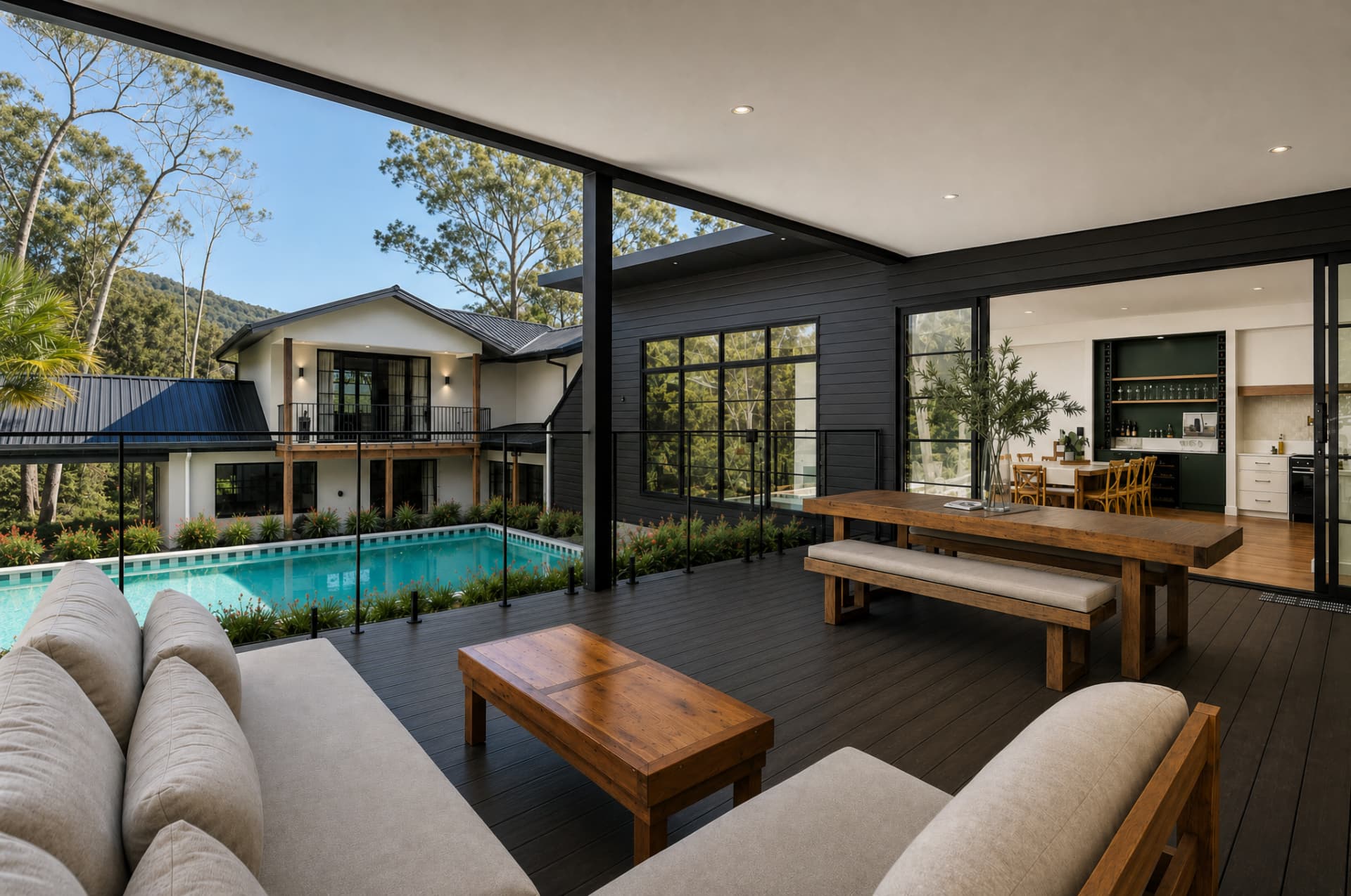 Covered outdoor deck and pool area of a custom Gold Coast home by All Leonard Build, with timber dining setting and bushland views.