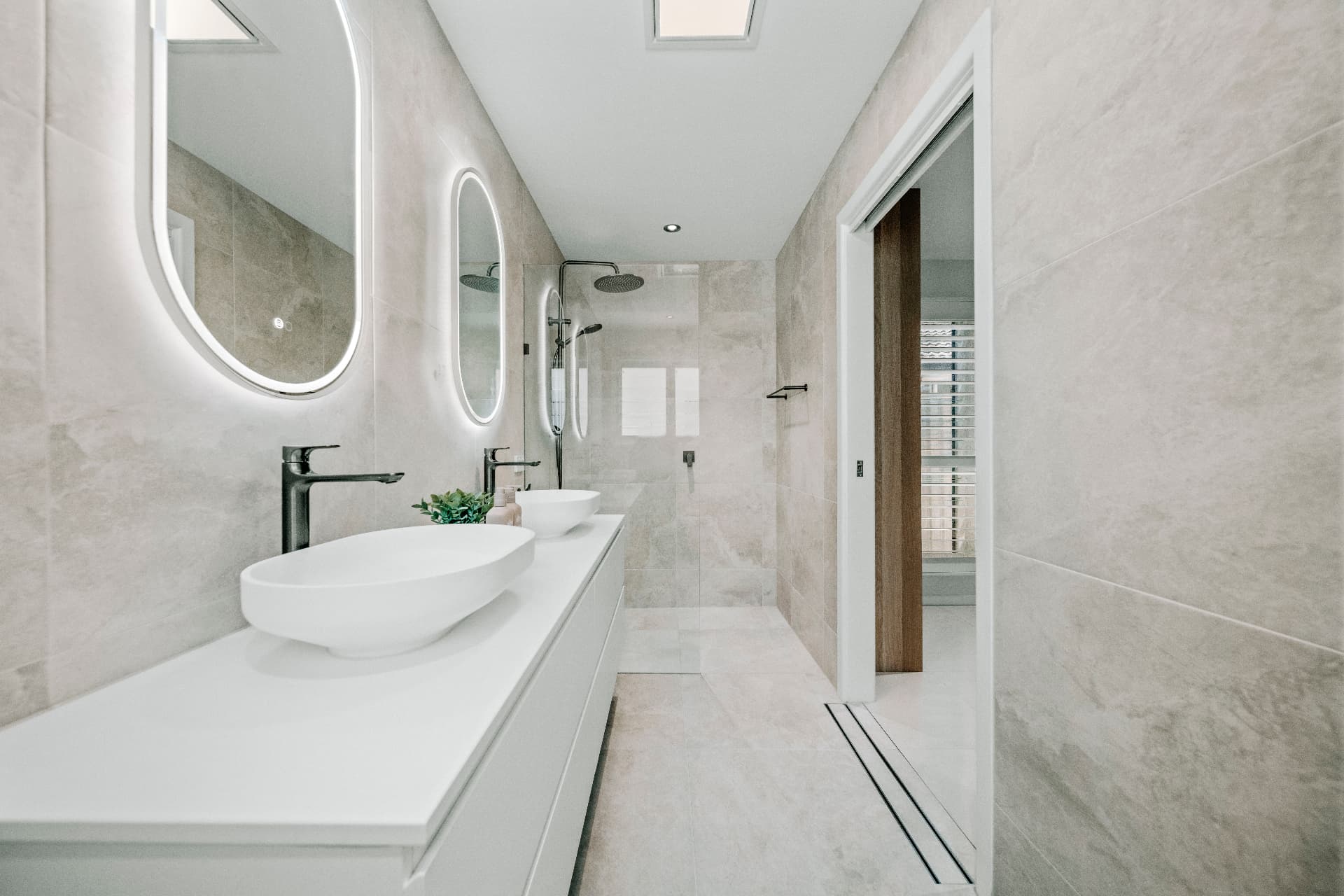 Mermaid Waters second dwelling main bathroom with twin oval mirrors, vessel basins and stone-look tiling.