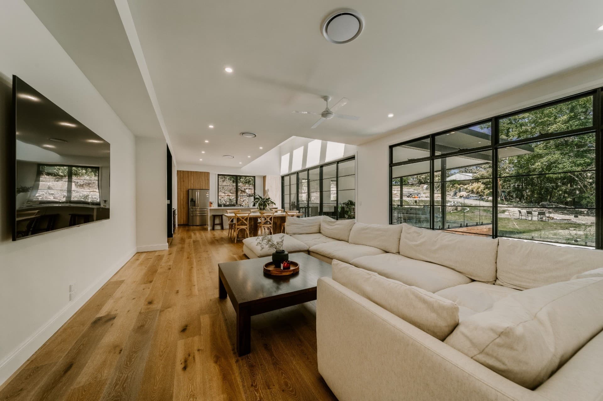 Yandala open plan living with sectional sofa, timber floors and steel-framed glazing.
